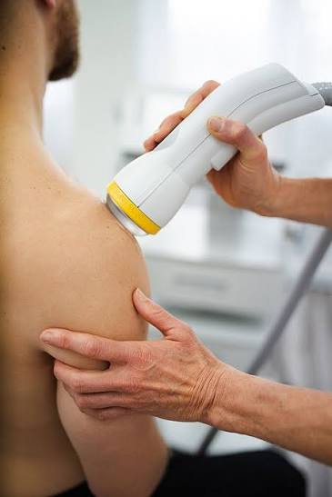 A clinician's gloved hand holding a SoftWave shockwave therapy applicator emitting a blue glow